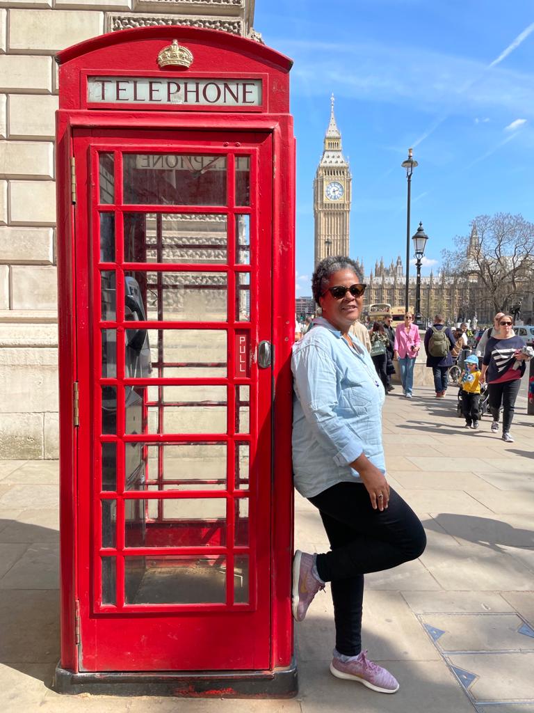 Flavia ao lado de uma cabine telefônica em Londres, com o Big Ben ao fundo